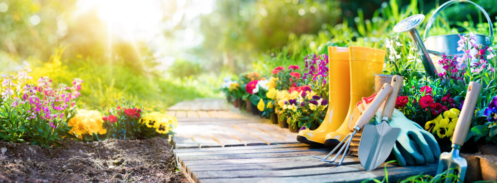Tuinpad met kleurrijke bloemen, tuingereedschap en gele regenlaarzen, perfect voor het creëren van verhoogde borders en een levendige tuin.