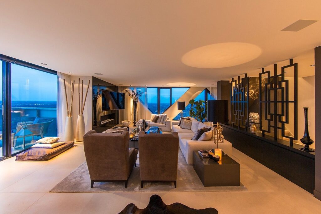 Een luxueuze woonkamer met warme tinten, stijlvolle meubels en een adembenemend uitzicht door kamerhoge ramen. Het perfecte samenspel van comfort en elegantie.