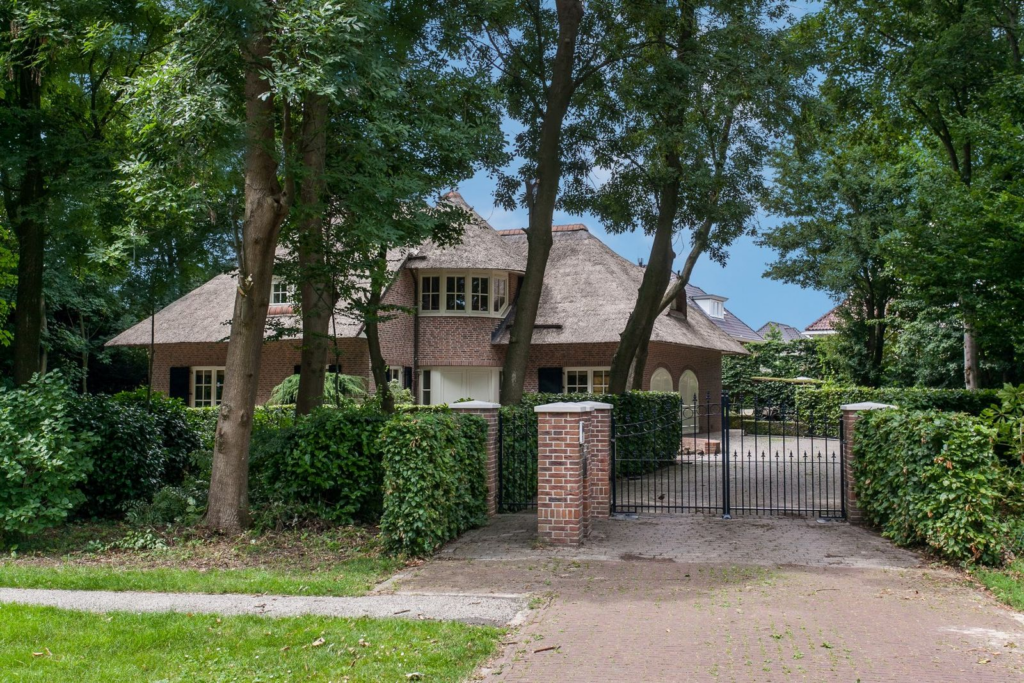Exclusieve villa met rieten kap in villawijk Bosweide, Den Haag, omgeven door groen en met een elektrische toegangspoort.