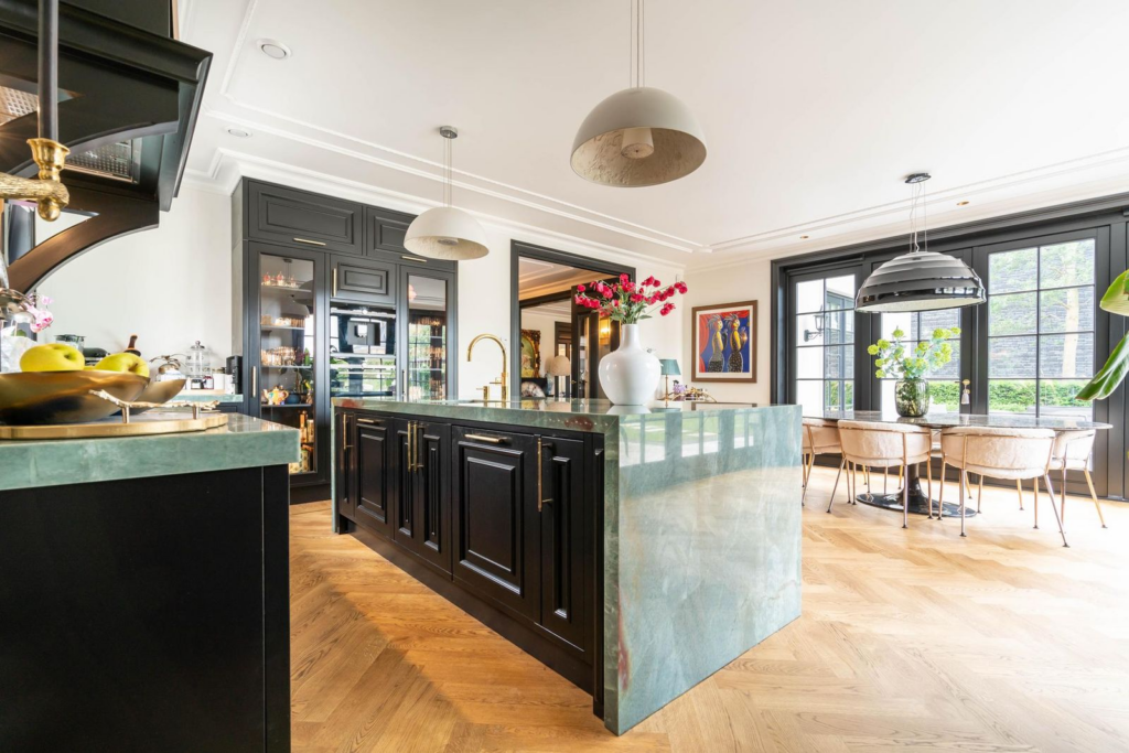 Luxe woonkeuken met een lichtgroen quartz werkblad, zwarte keukenkasten en grote raampartijen in een exclusieve villa in Den Haag.