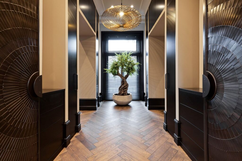 Een prachtig ingerichte hal met elegante details, warme houten vloeren en moderne afwerkingen. De centraal geplaatste olijfboom voegt een vleugje natuur toe aan het strakke, luxueuze interieur.