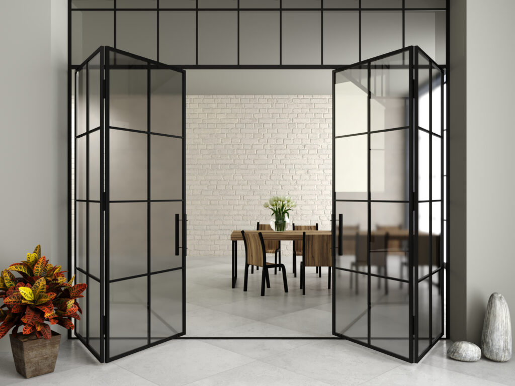 Dubbele stalen binnendeuren met glas in een moderne woning, gescheiden van een eetkamer met een lichte bakstenen muur en houten tafel.