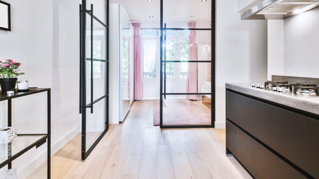 Zwarte stalen binnendeur met glas, geplaatst tussen een moderne keuken en een lichte ruimte met roze accenten, benadrukt het ruimtelijke en stijlvolle interieur