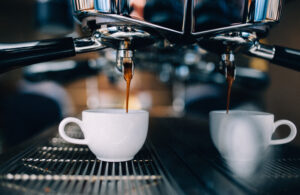 Close-up van een professionele espressomachine die twee kopjes koffie zet. De donkere koffie stroomt uit de machine in witte koffiekopjes, wat zorgt voor een sfeervolle en uitnodigende setting.
