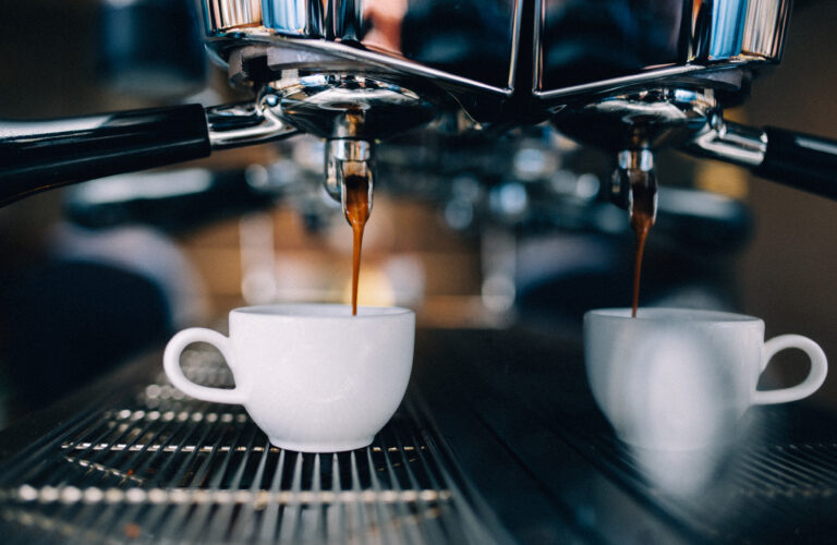 Close-up van een professionele espressomachine die twee kopjes koffie zet. De donkere koffie stroomt uit de machine in witte koffiekopjes, wat zorgt voor een sfeervolle en uitnodigende setting.
