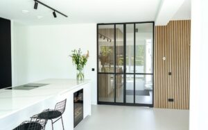 Moderne keuken met een stalen binnendeur voorzien van glas, gecombineerd met houten wandbekleding en een licht interieurontwerp
