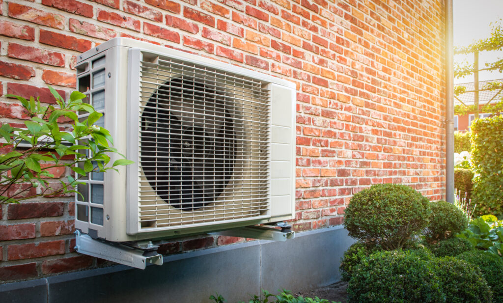 Warmtepompunit aan de buitenmuur van een woning, omgeven door groen, als voorbeeld van duurzame en energiezuinige verwarming.