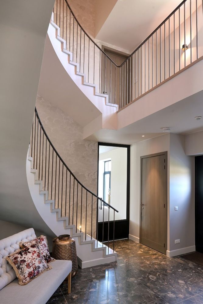 Stijlvol trappenhuis met een betonnen trap, strakke balustrades en een marmeren vloer in een luxe woning.