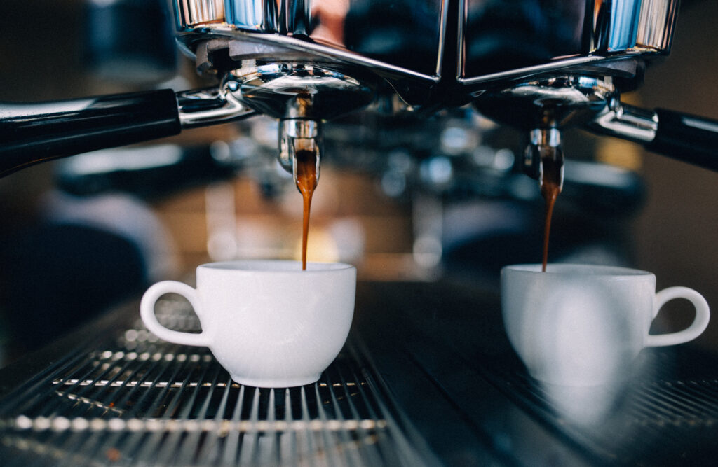 Close-up van een espressoapparaat dat koffie zet in twee kopjes, wat het belang van onderhoud en waterkwaliteit benadrukt voor huishoudelijke apparaten.