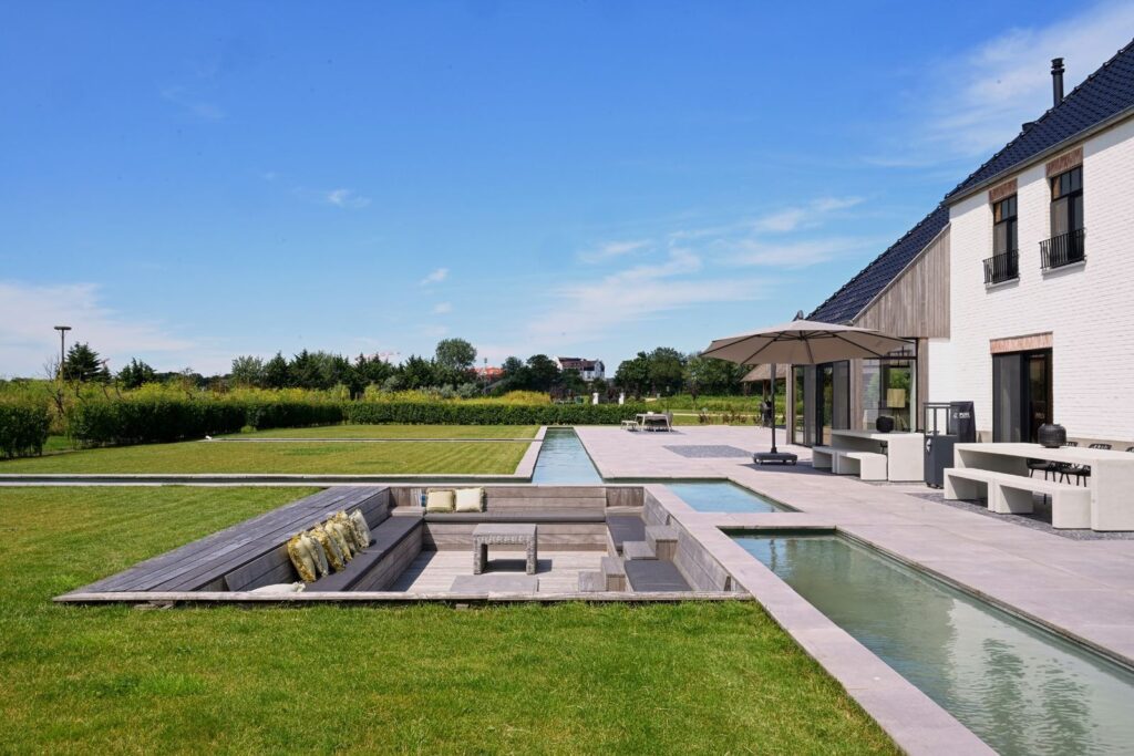 Moderne tuin met verzonken loungehoek, waterpartijen en ruim terras bij een luxe landhuis in Cadzand