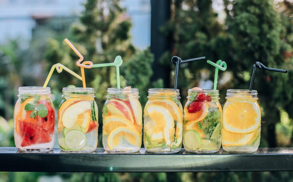 Zomerse drankjes in glazen potjes met fruit, ijsblokjes en rietjes op een tuintafel