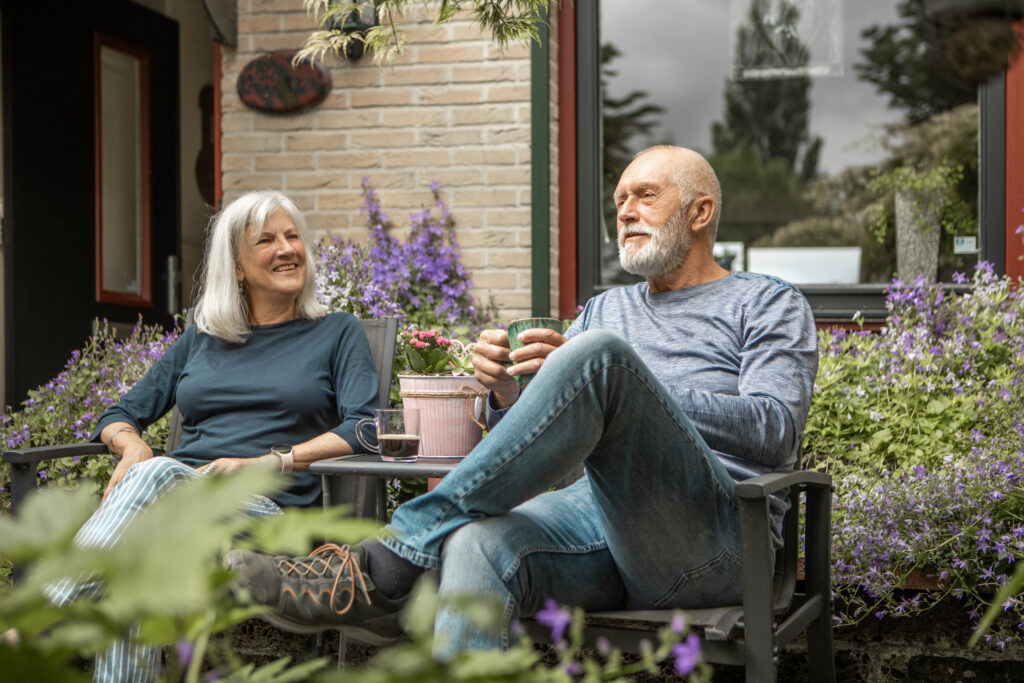 Seniorenpaar geniet van een kleurrijke voortuin vol bloemen en groen voor hun huis