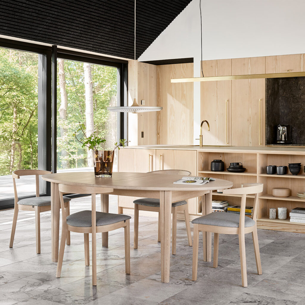 Ronde uitschuifbare eettafel van licht hout in moderne open keuken met uitzicht op het bos