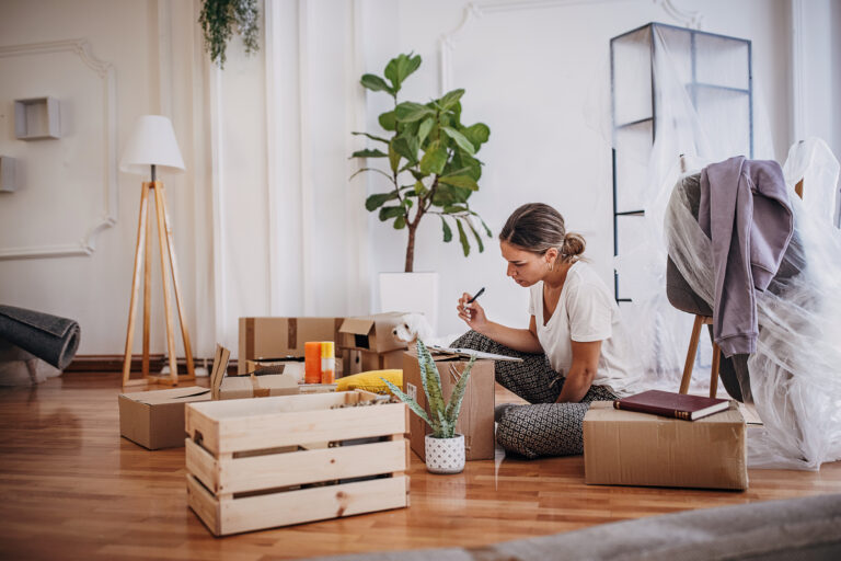 Vrouw maakt verhuischecklist te midden van verhuisdozen in haar nieuwe woning