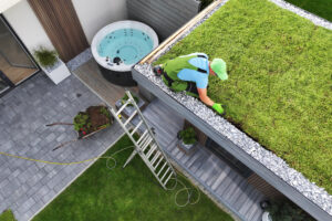 Man werkt aan groendak van modern bijgebouw in strakke tuin met jacuzzi