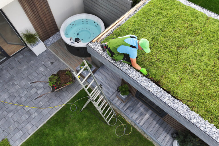 Man werkt aan groendak van modern bijgebouw in strakke tuin met jacuzzi