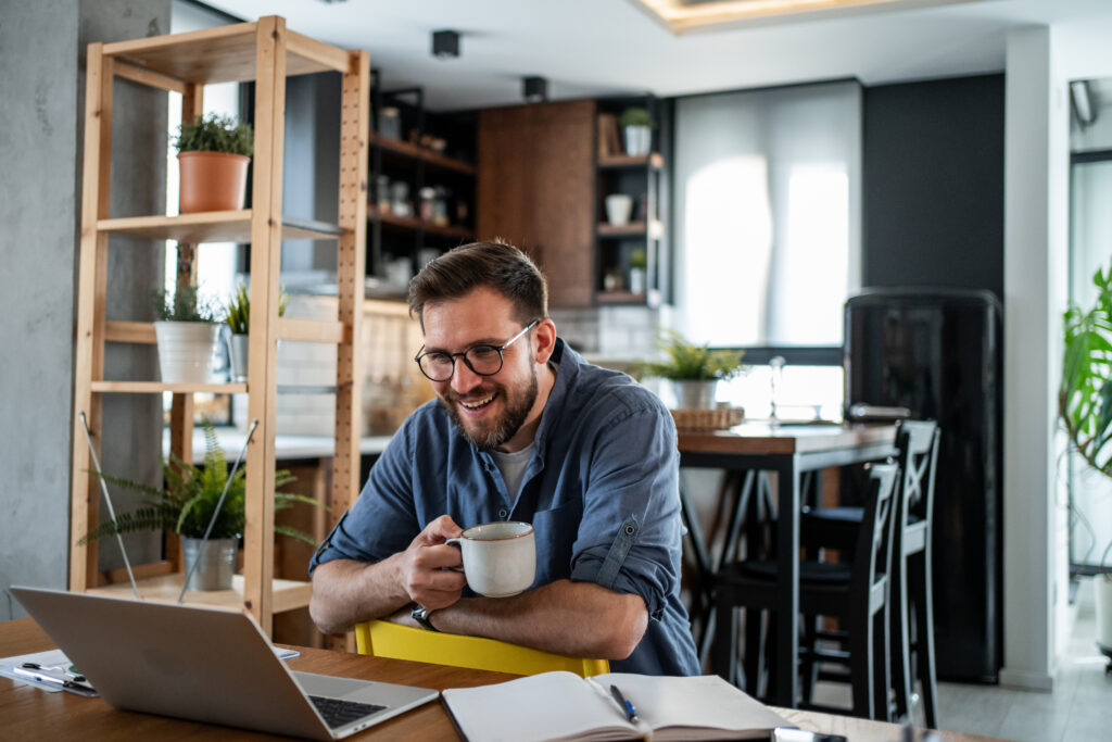Man werkt vanuit huis aan de keukentafel met laptop en kop koffie