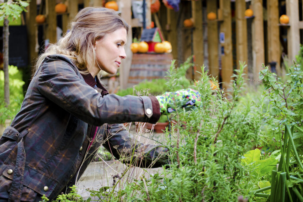 Vrouw verzorgt planten in een groene tuin met handschoenen en jas