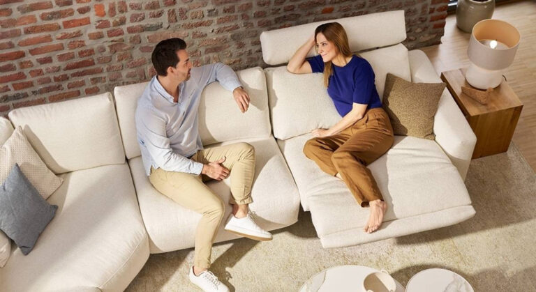 Stel dat samen verschillende posities test op een beige relaxbank in een lichte woonkamer.