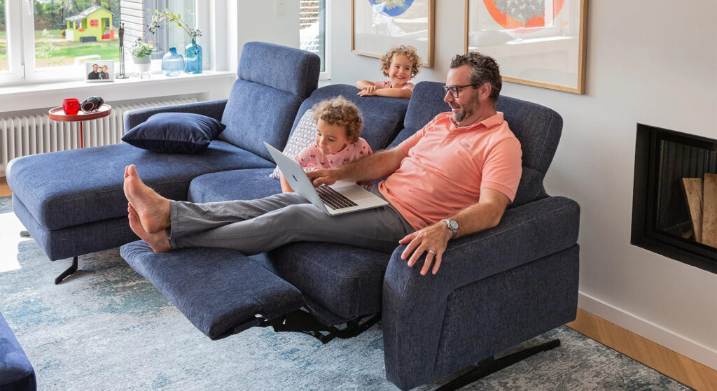 Vader en twee kinderen ontspannen op een blauwe relaxbank met uitgeklapte voetensteun.