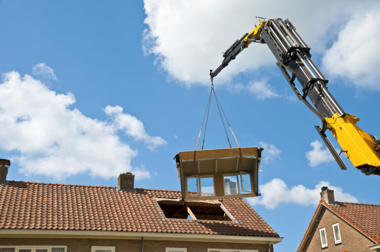 Hijskraan plaatst prefab dakopbouw op een woning tijdens werkzaamheden op hoogte.
