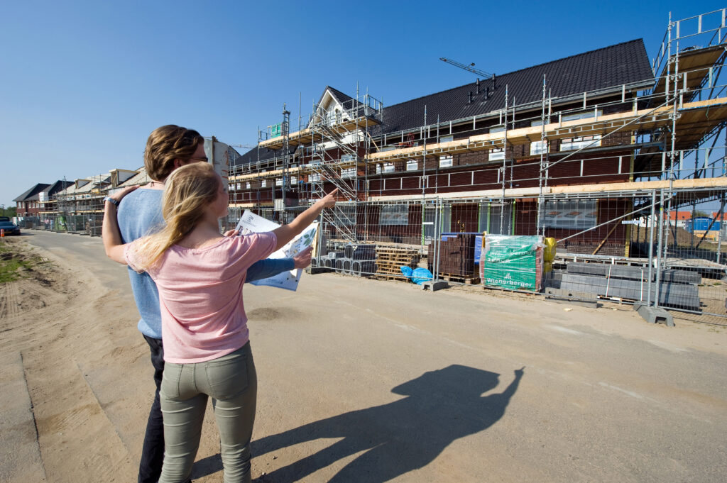 Overleg op de bouwplaats bij woningen in aanbouw, met aandacht voor planning en werkzaamheden op hoogte.