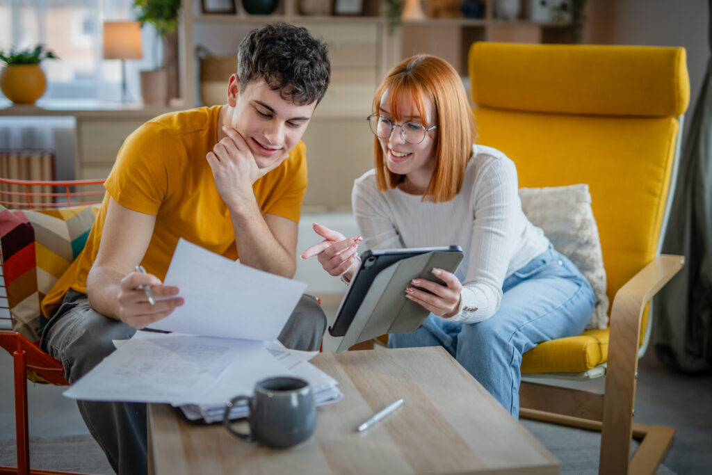 Jong stel bekijkt papieren en tablet om te berekenen hoeveel spaargeld nodig is voor een huis